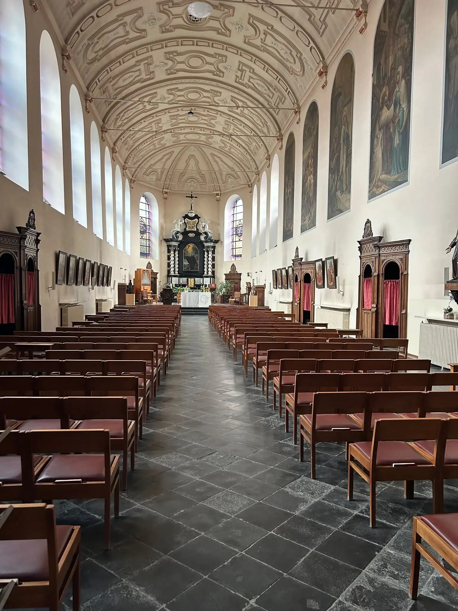 Middenbeuk van de Minderbroederskerk in Hasselt met rijen houten stoelen, het barokke tongewelf en het altaar