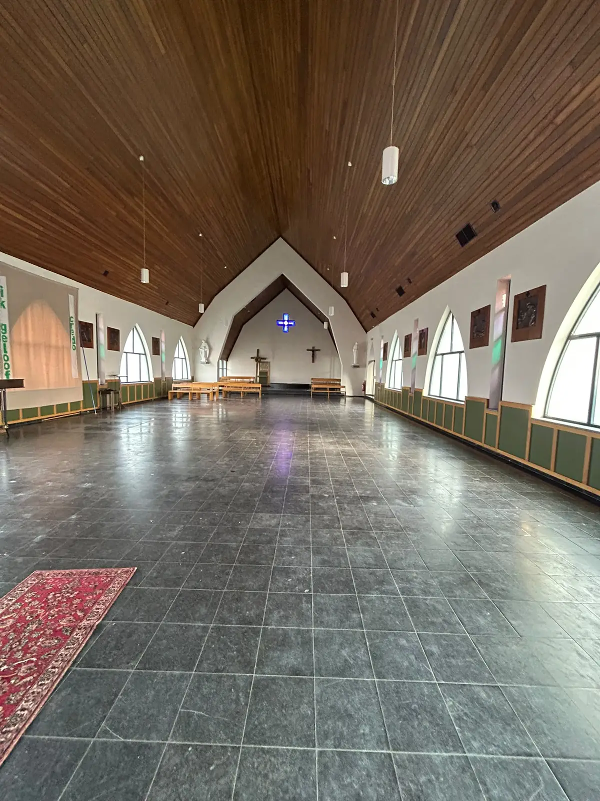 Lege kerkzaal met houten plafond, spitsboogramen en een blauw glas-in-loodkruis