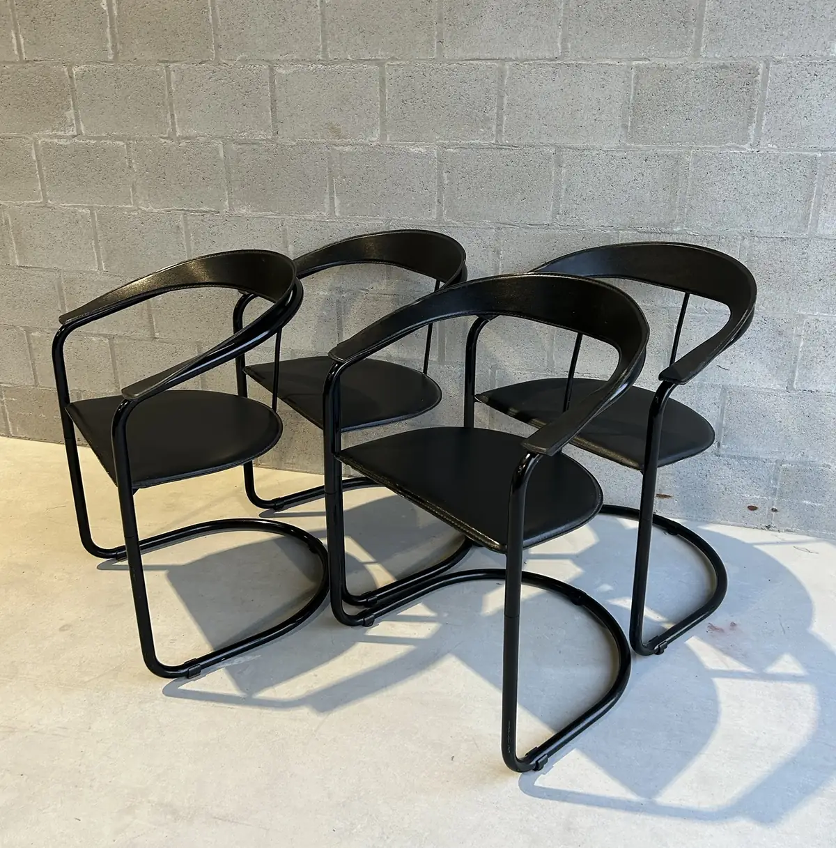 Vier vintage designstoelen van zwart leder met een buisframe